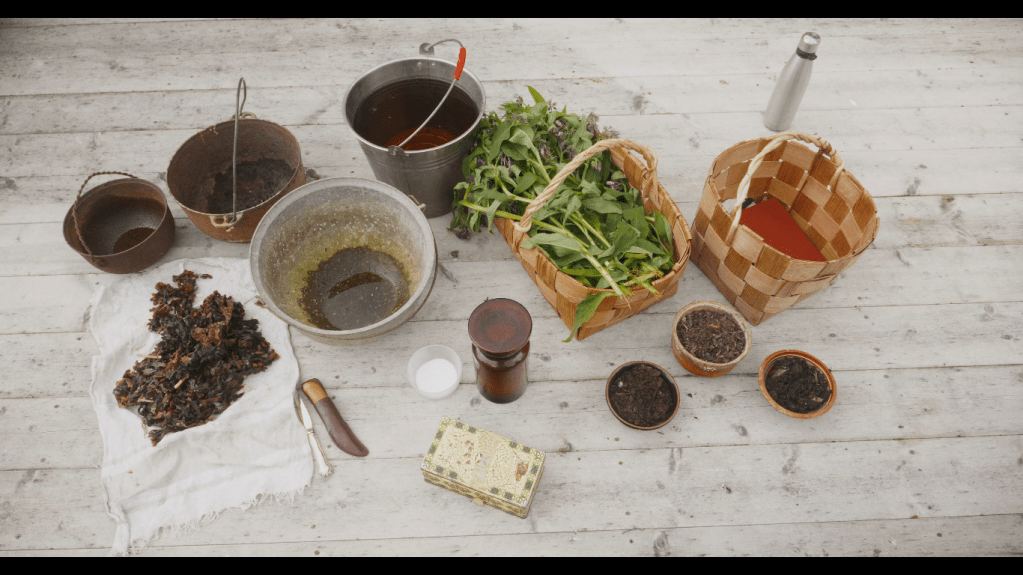 Pictured part of Inkeri Kurkilahti's Biochar Witchcraft -performance. There are different kinds of potions, baskets, herbs, cauldrons and various assortments on a wooden deck.